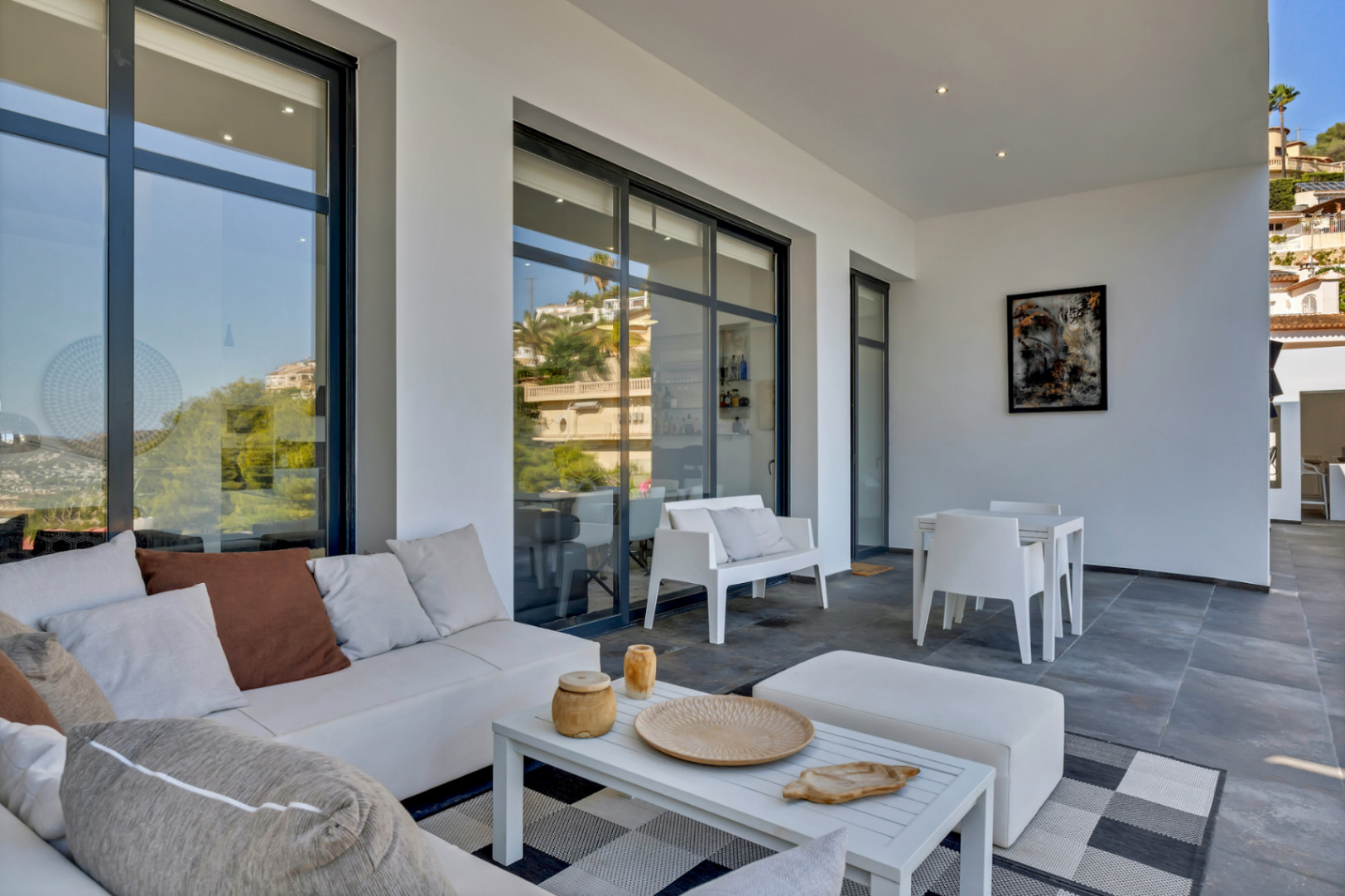 Terraza cubierta con zona de estar de diseño, suelos de gres gris y grandes ventanales de carpintería negra que reflejan el entorno residencial.