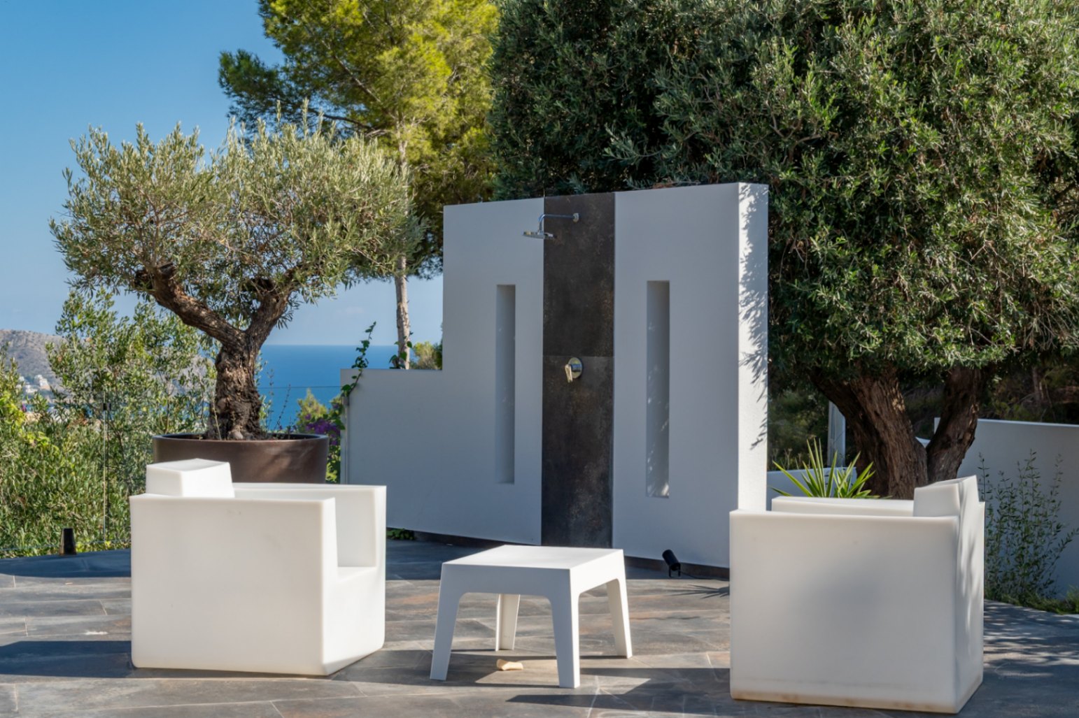 Zona de relax exterior con mobiliario de diseño minimalista, ducha integrada en muro arquitectónico y vistas despejadas al mar Mediterráneo.