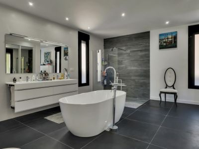 Luminoso baño con bañera exenta blanca, lavabo suspendido con espejo y suelo de baldosas grises.
