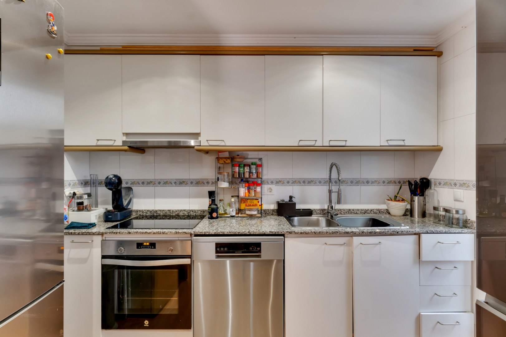 Cocina equipada con armarios blancos, encimera de granito y electrodomésticos de acero inoxidable como horno y lavavajillas integrados.
