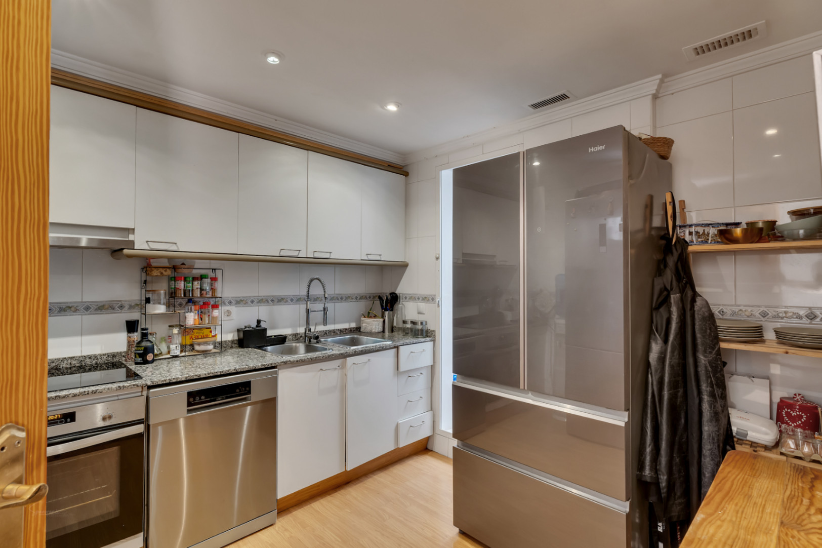 Cocina funcional equipada con armarios blancos, encimera de granito y electrodomésticos de acero inoxidable, incluyendo un frigorífico de gran capacidad y lavavajillas.