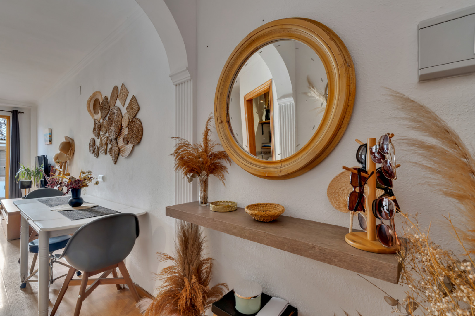 Entrada acogedora con espejo circular de madera, estante flotante y decoración de fibras naturales que conecta con un comedor de planta abierta.