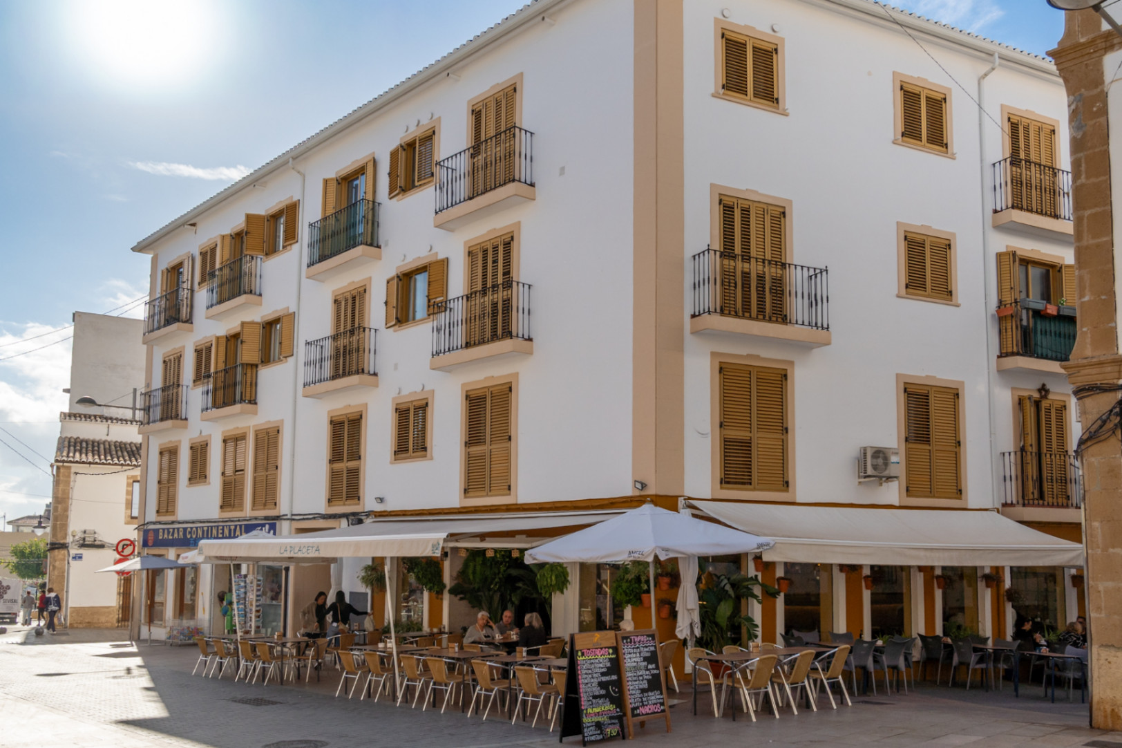 Fachada de edificio tradicional en el casco antiguo de Jávea con balcones de forja, contraventanas de madera y una terraza de cafetería en la planta baja.