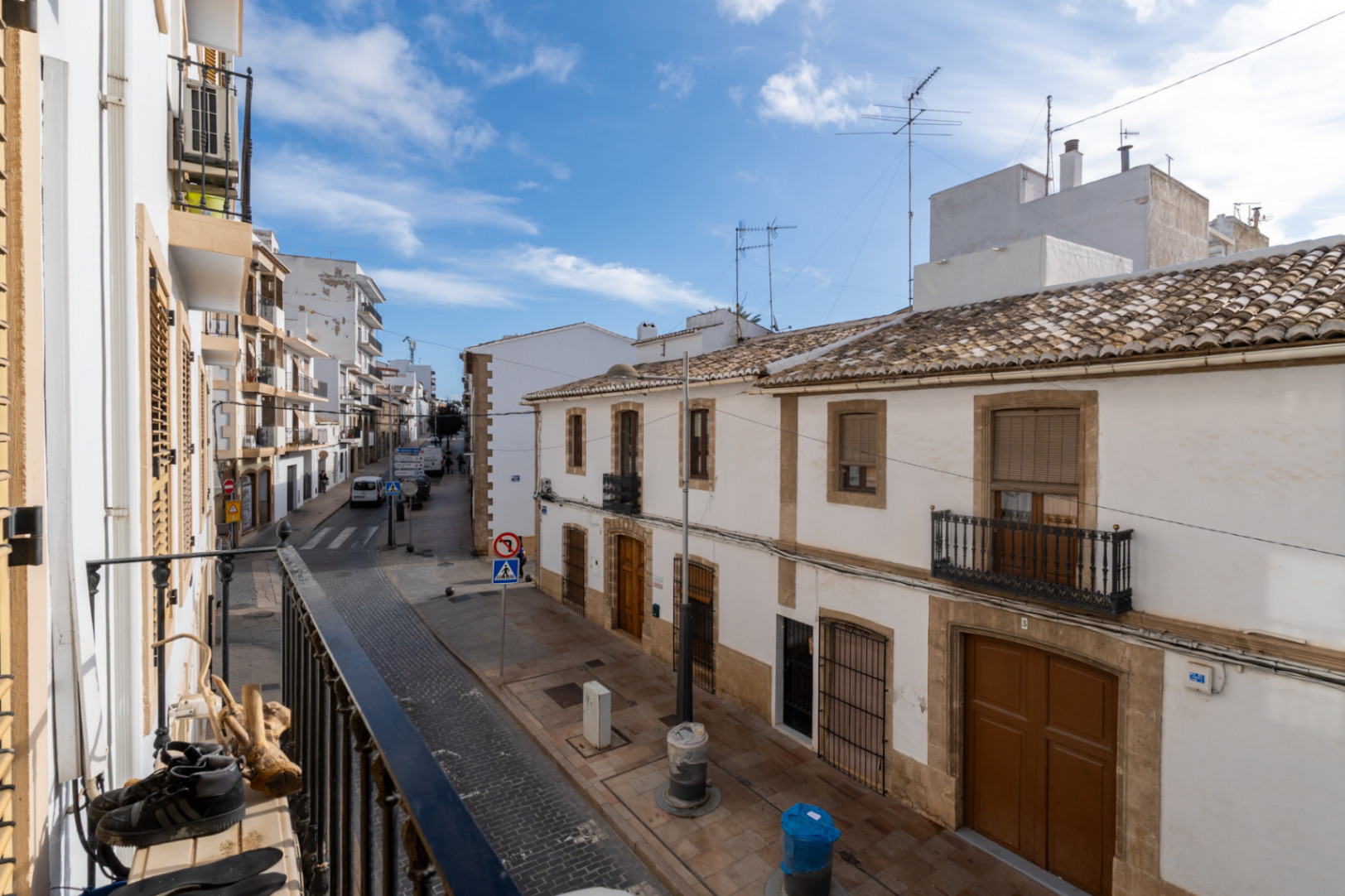 Vista desde el balcón hacia una calle del casco antiguo de Jávea, mostrando fachadas blancas tradicionales con marcos de piedra tosca y tejados de arcilla bajo un cielo despejado.