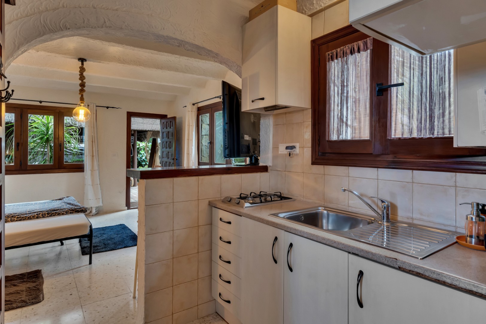 Cocina compacta del apartamento de invitados con encimera de piedra, hornilla de gas y fregadero de acero, integrada bajo techos abovedados con texturas tradicionales.