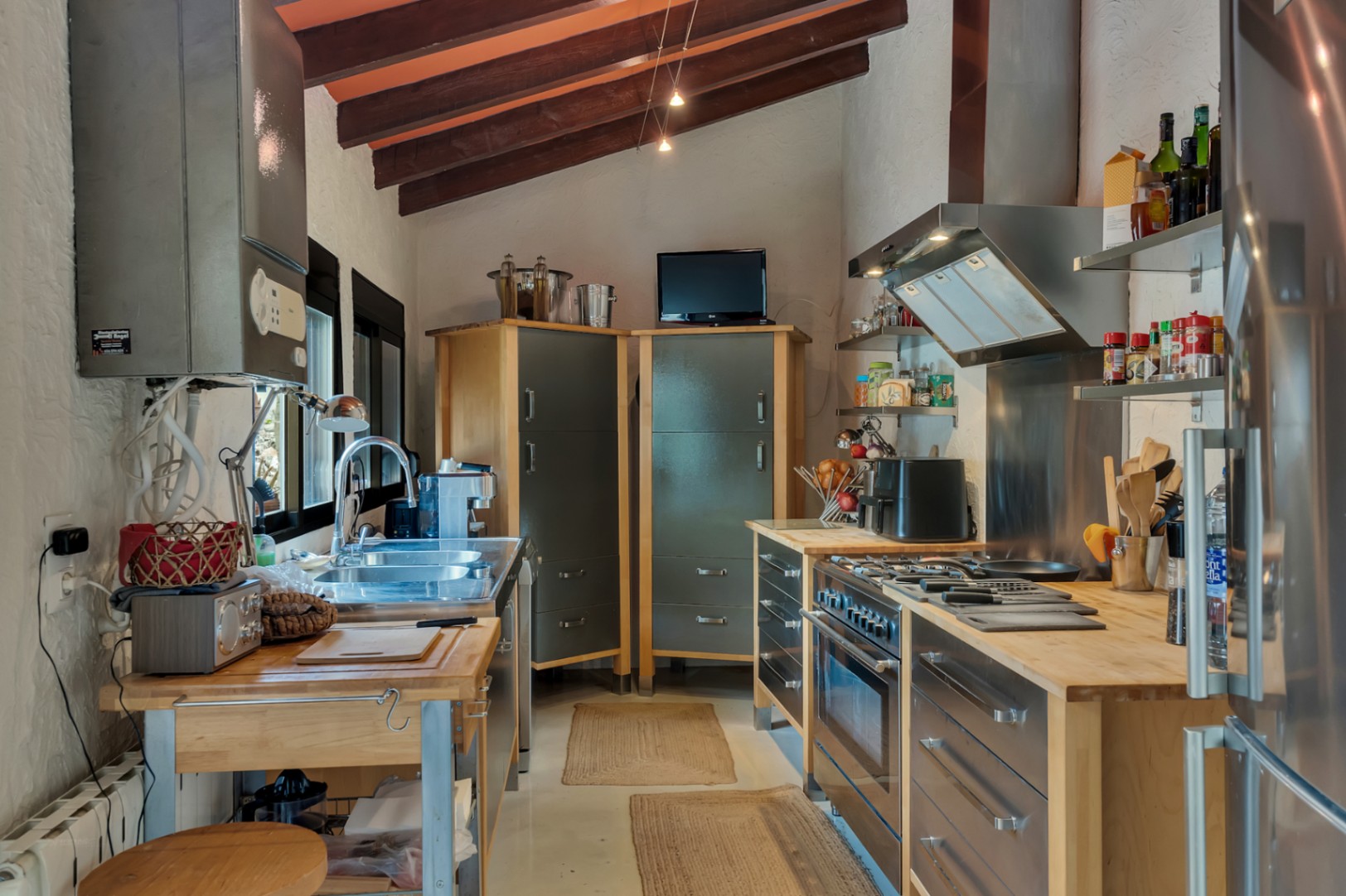Cocina de diseño industrial con techos de vigas de madera vista, encimeras de madera maciza y electrodomésticos de acero inoxidable integrados en un espacio funcional.