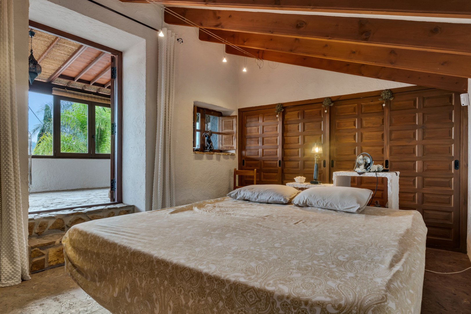 Dormitorio con techos de vigas de madera vista, armarios empotrados de estilo tradicional y acceso directo a una terraza cubierta mediante un escalón de piedra.
