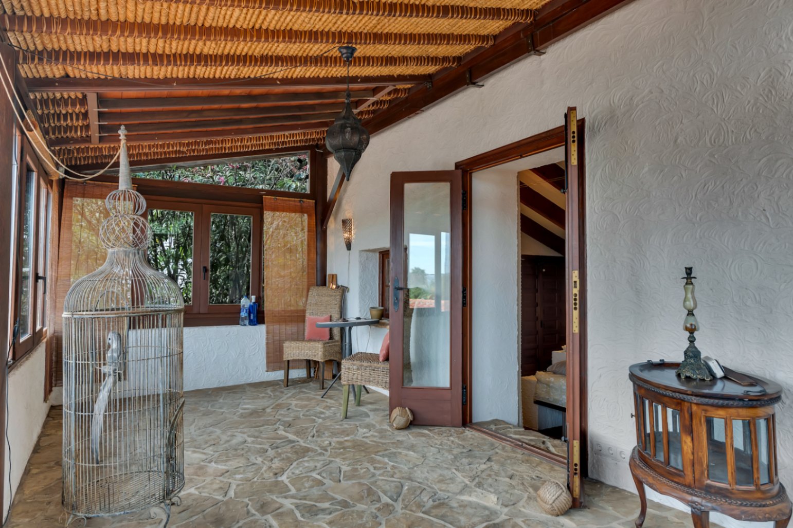Naya tradicional con suelo de piedra natural, techo de vigas de madera y cañizo. Incluye mobiliario de mimbre y acceso directo al interior mediante puertas acristaladas.