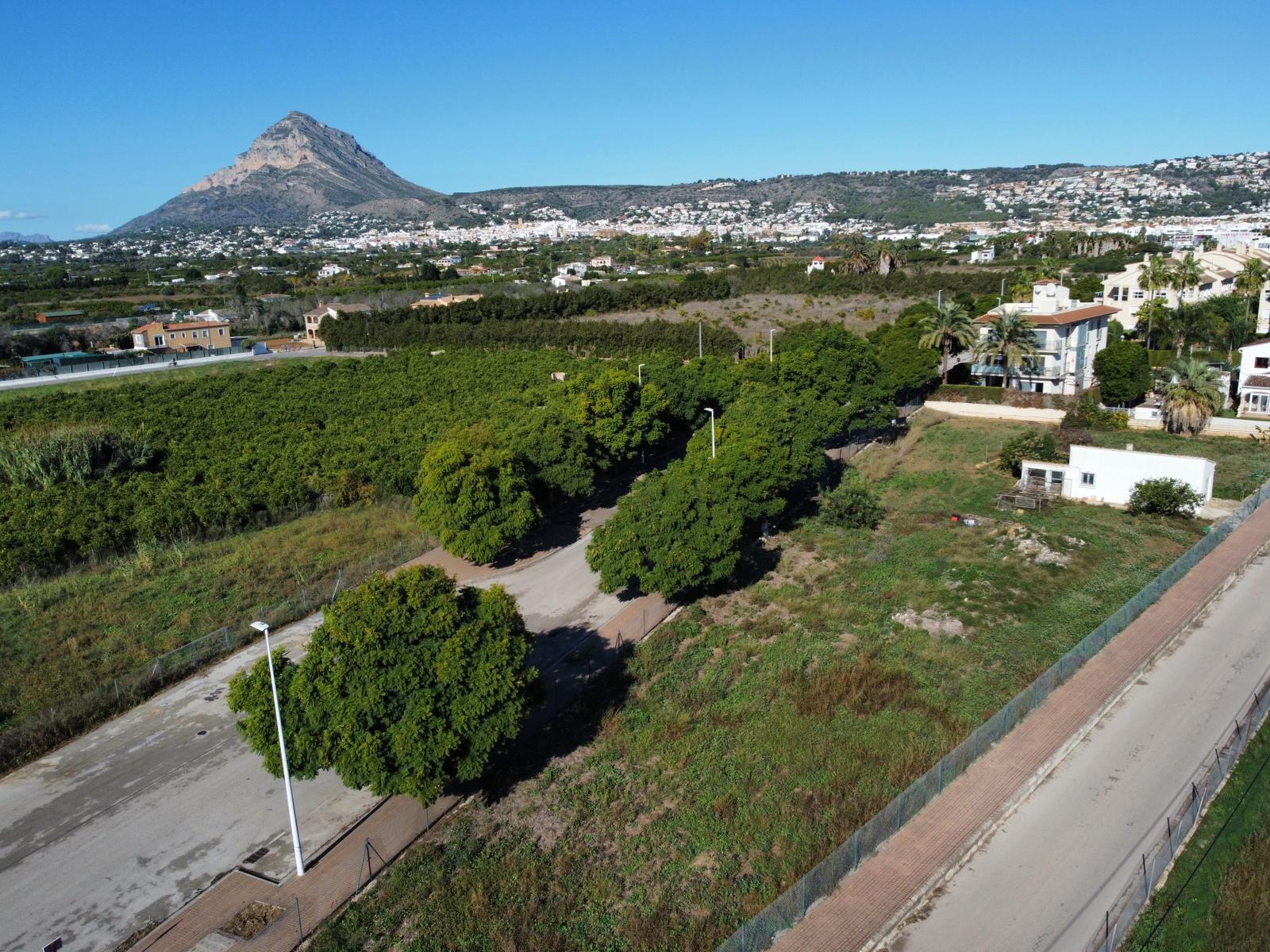 Vista aérea de la parcela residencial en Jávea, destacando el acceso asfaltado y el emblemático macizo del Montgó al fondo bajo un cielo despejado.