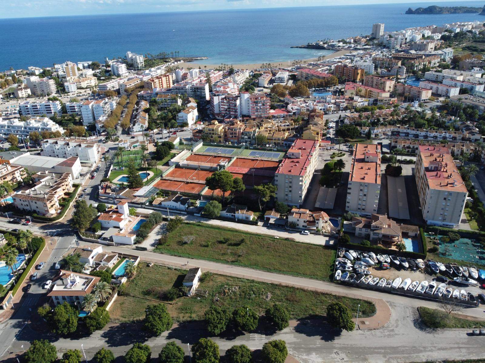 Vista aérea del solar urbano en Jávea, destacando su ubicación estratégica junto al club de tenis y la cercanía a la Playa del Arenal con vistas al mar.