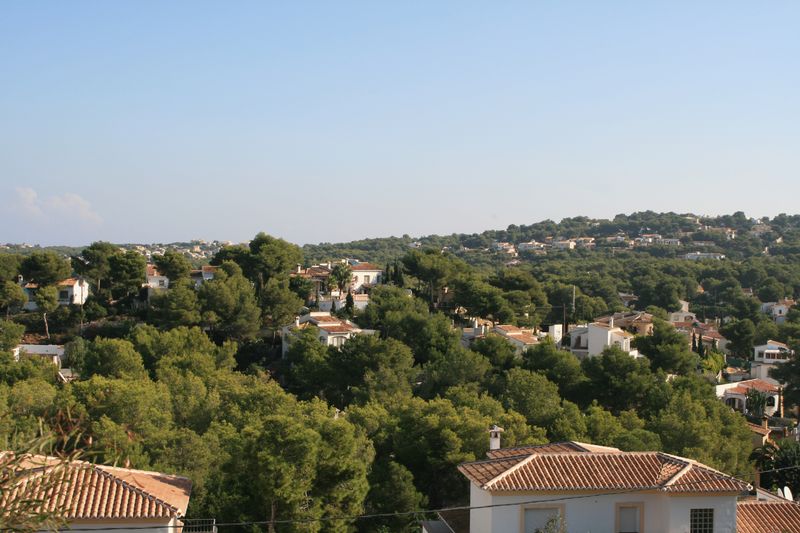 Vista panorámica desde la parcela hacia una zona residencial consolidada, rodeada de densos pinares mediterráneos y villas de estilo tradicional bajo un cielo despejado.
