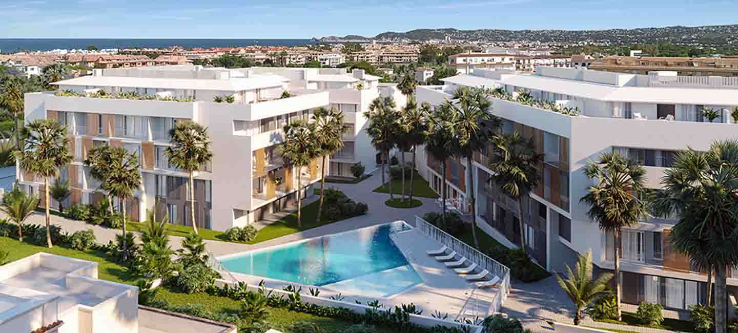 Vista aérea del complejo de apartamentos contemporáneos con edificios blancos, contraventanas de madera, una piscina triangular y jardines con palmeras.