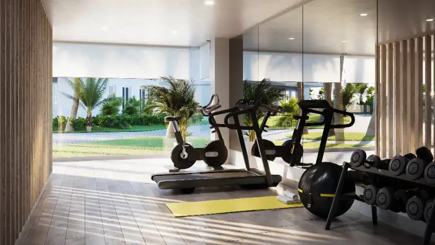 Gimnasio moderno con equipos de cardio, pesas libres y ventanales con vistas a los jardines mediterráneos. Incluye paredes de listones de madera e iluminación empotrada.