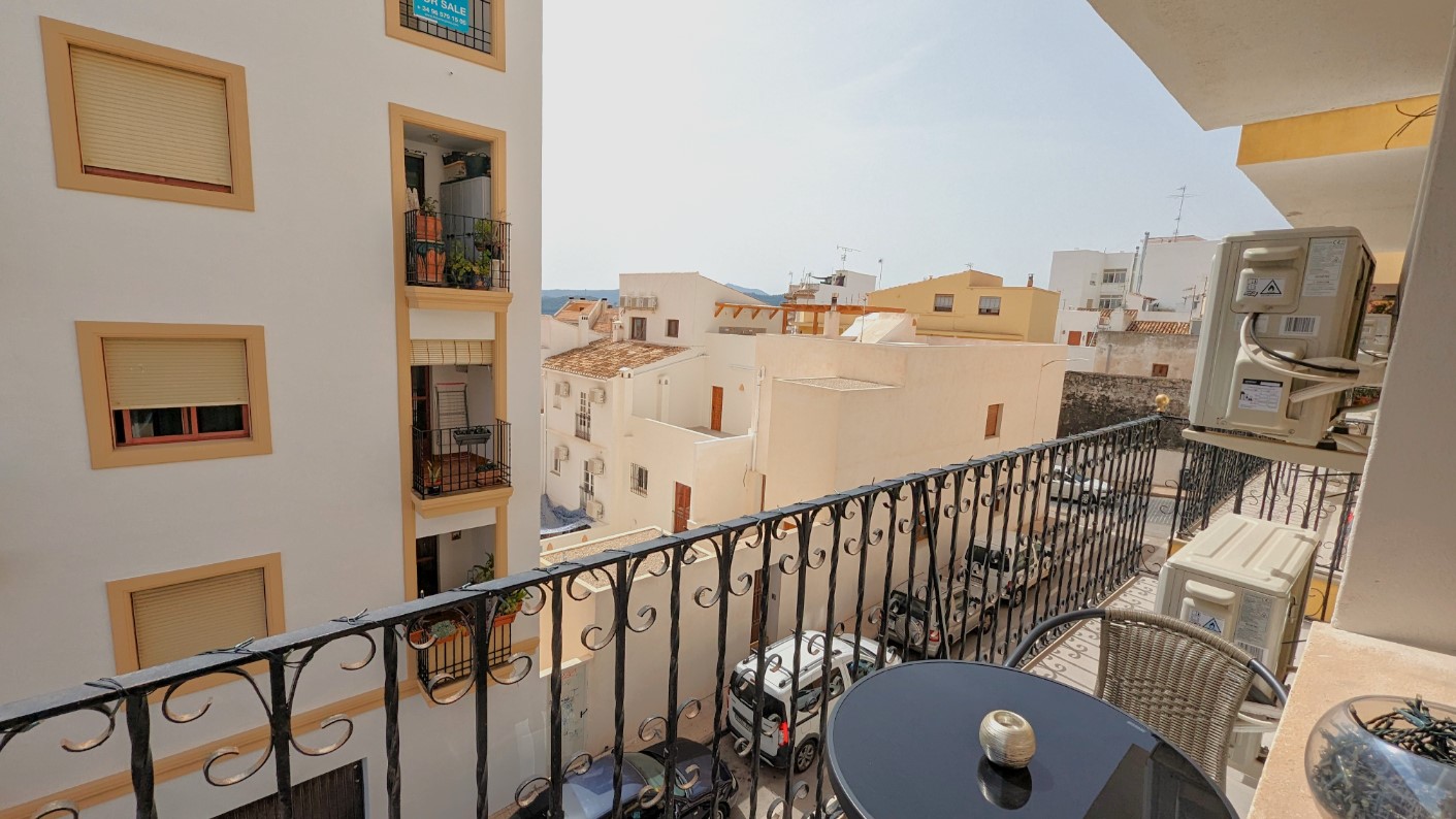 Balcón privado con barandilla de hierro forjado, equipado con mesa auxiliar y vistas a las calles y edificios tradicionales del casco antiguo de Jávea.