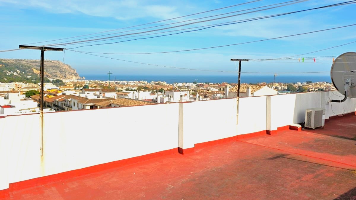 Terraza comunitaria en la azotea con suelo de baldosa roja y vistas panorámicas del casco antiguo de Jávea y el mar Mediterráneo.