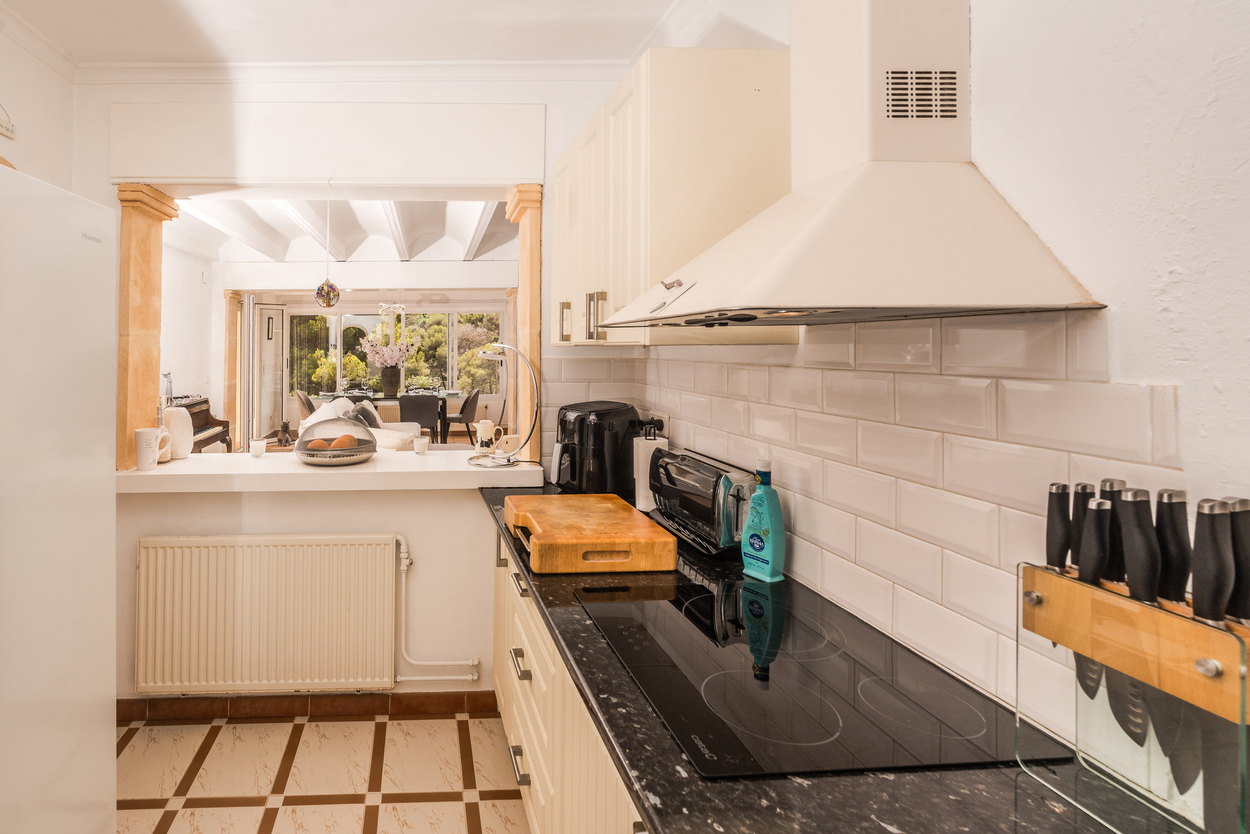 Cocina equipada con encimeras de granito oscuro, azulejos tipo metro y barra americana que conecta con el salón a través de pilares de piedra tosca.