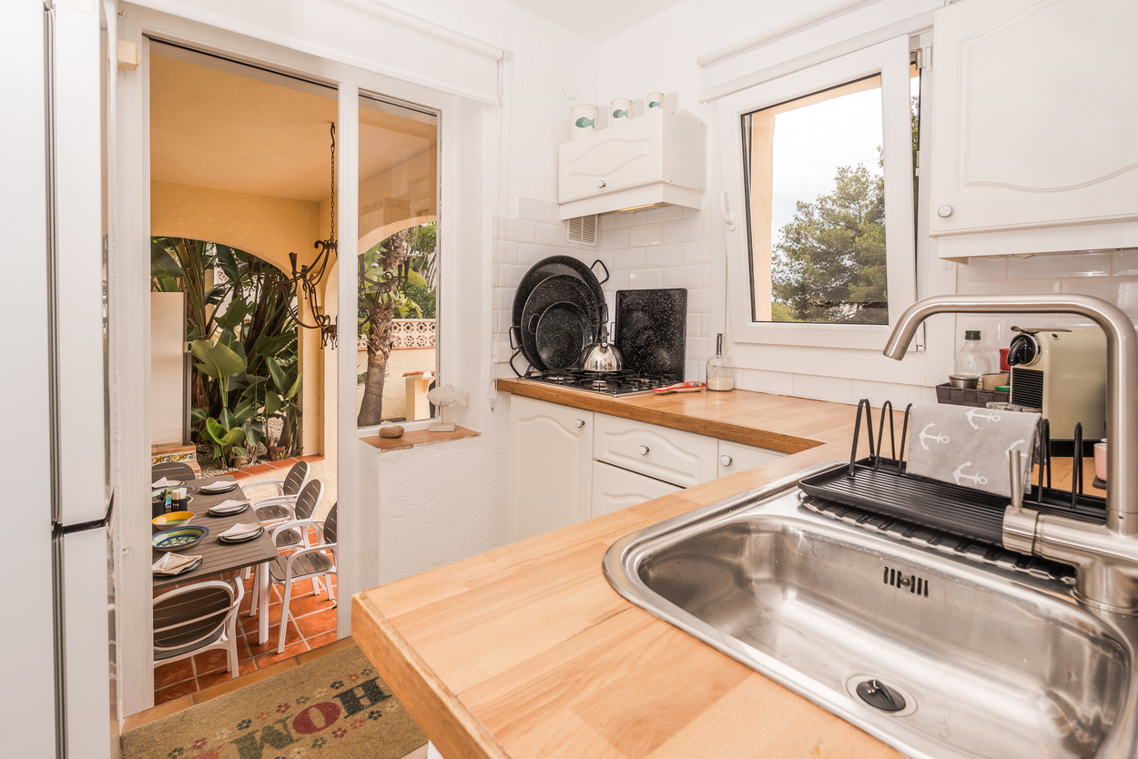 Cocina equipada con encimeras de madera, azulejos tipo metro y acceso directo a una naya exterior con zona de comedor bajo arcos mediterráneos.