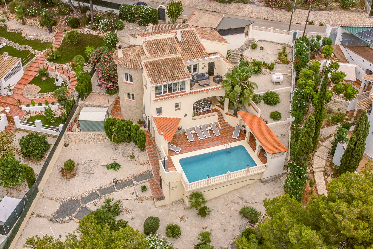 Vista aérea de la villa con su piscina de 8x4m, amplias terrazas de terracota y torre de piedra natural, integrada en un jardín mediterráneo autóctono.