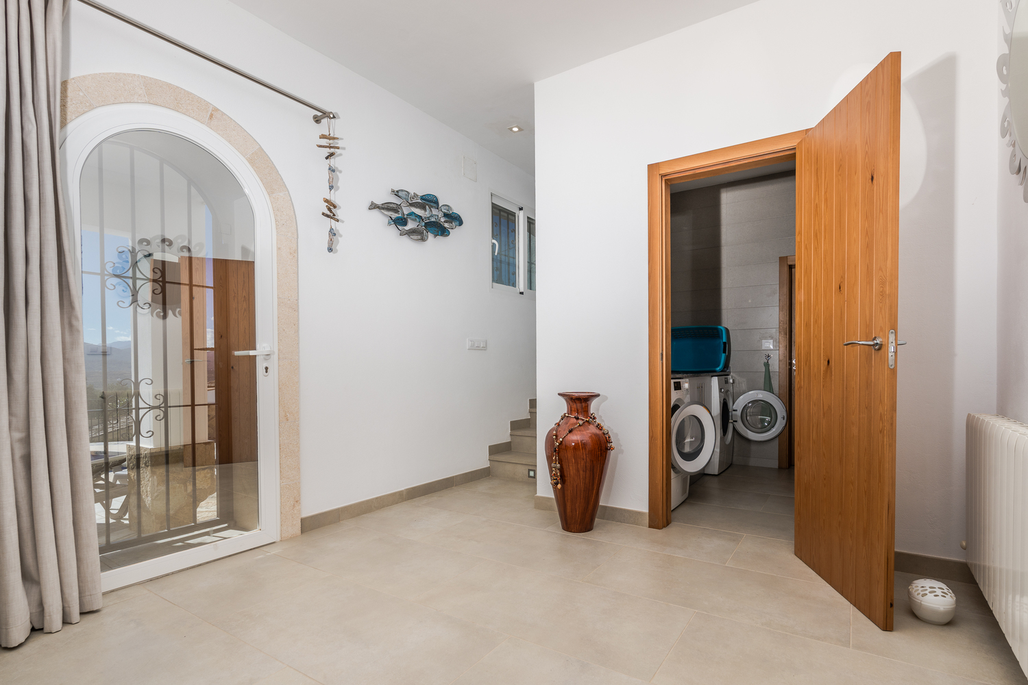 Distribuidor con suelos cerámicos, puerta de cristal en arco con marco de piedra y acceso a un lavadero equipado a través de una puerta de madera.