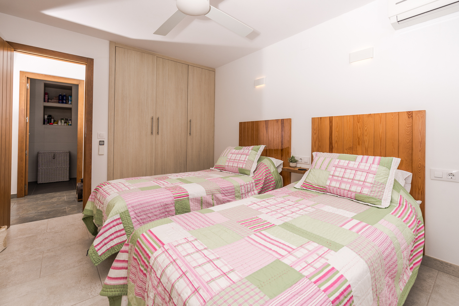Dormitorio luminoso con dos camas individuales, cabeceros de madera natural, armarios empotrados y acceso directo a un baño privado.