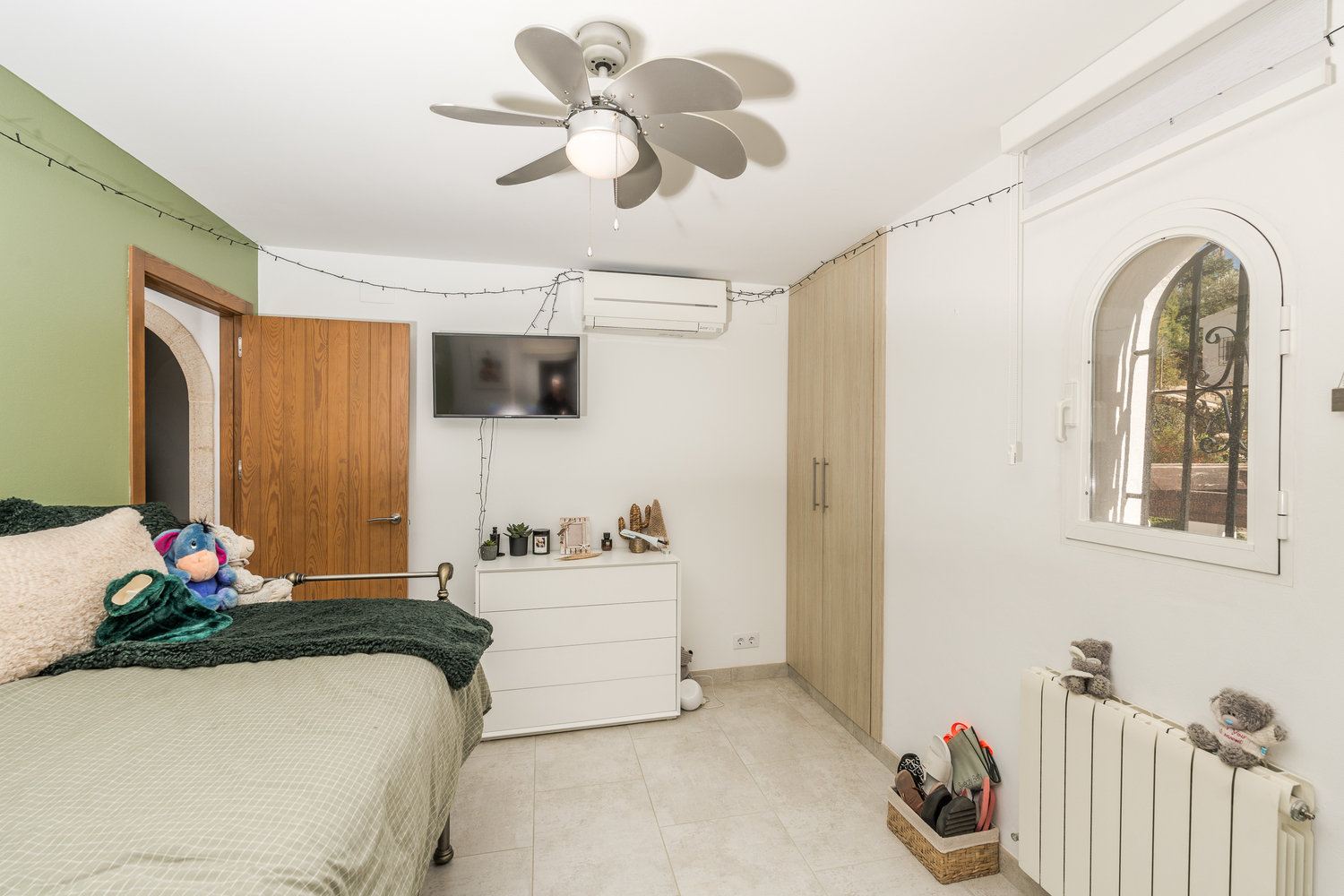 Dormitorio luminoso con pared de acento verde, armarios empotrados y ventana de arco. Equipado con aire acondicionado, ventilador de techo y calefacción central.