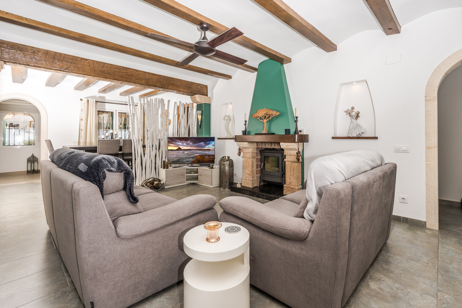 Salón con vigas de madera vistas, chimenea de piedra con estufa de leña integrada y suelos cerámicos de tonos naturales.