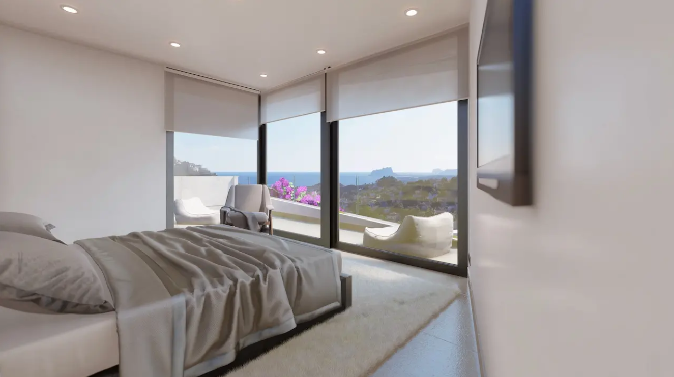 Dormitorio moderno con ventanales de suelo a techo, vistas panorámicas al Mediterráneo y al Peñón de Ifach, y acceso directo a una terraza privada.