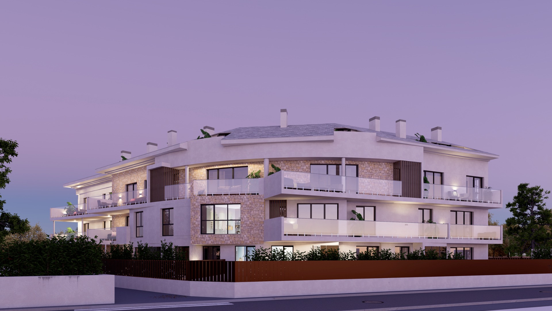 Vista exterior del edificio de tres plantas al atardecer, con fachadas blancas, detalles en piedra natural y amplias terrazas con barandillas de cristal e iluminación cálida.