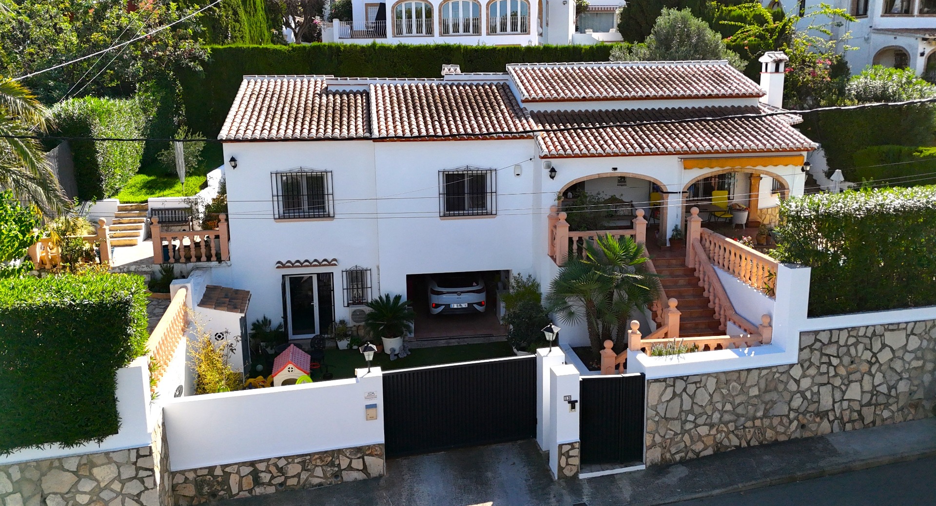 Vista exterior de una villa mediterránea de dos niveles con fachada blanca, tejado de terracota, garaje integrado y terraza con arcos y balaustradas de piedra.