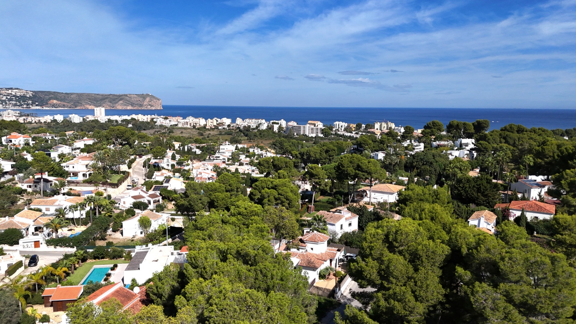 Vista panorámica elevada de la zona residencial de Toscal en Jávea, mostrando villas mediterráneas entre pinares con el Cabo de San Antonio al fondo.