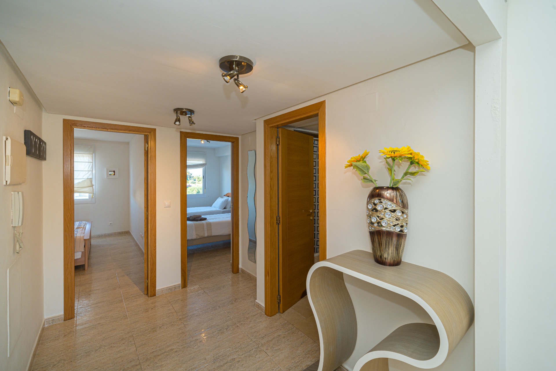 Pasillo central con suelos de gres pulido que conecta los dormitorios y el baño, equipado con focos modernos y una consola de diseño curvo.