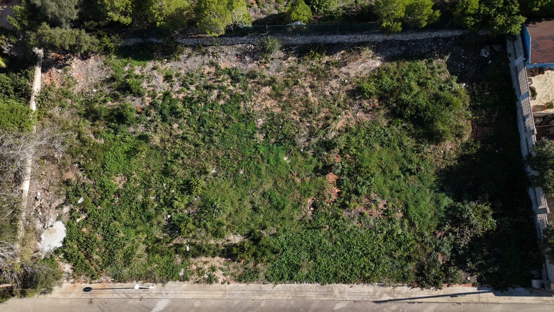 Vista aérea de la parcela llana de 889 m² en Pinosol, destacando su forma rectangular, vegetación natural y acceso directo desde la calle residencial pavimentada.
