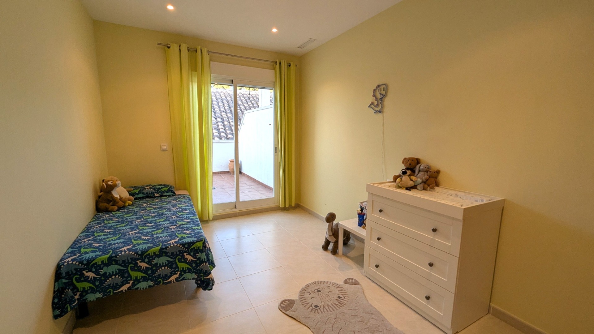 Dormitorio luminoso con suelos de gres, cortinas verde lima y acceso directo a una terraza privada a través de una puerta corredera de cristal.