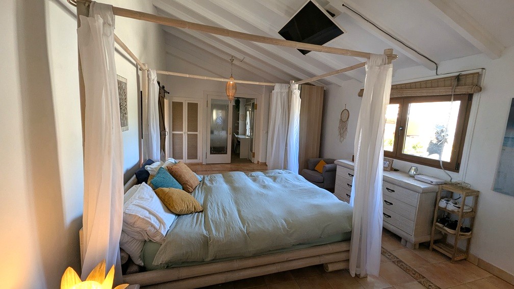 Dormitorio con cama de dosel de bambú, techos abovedados de vigas blancas y suelo de terracota. Dispone de televisión en el techo y armarios empotrados.