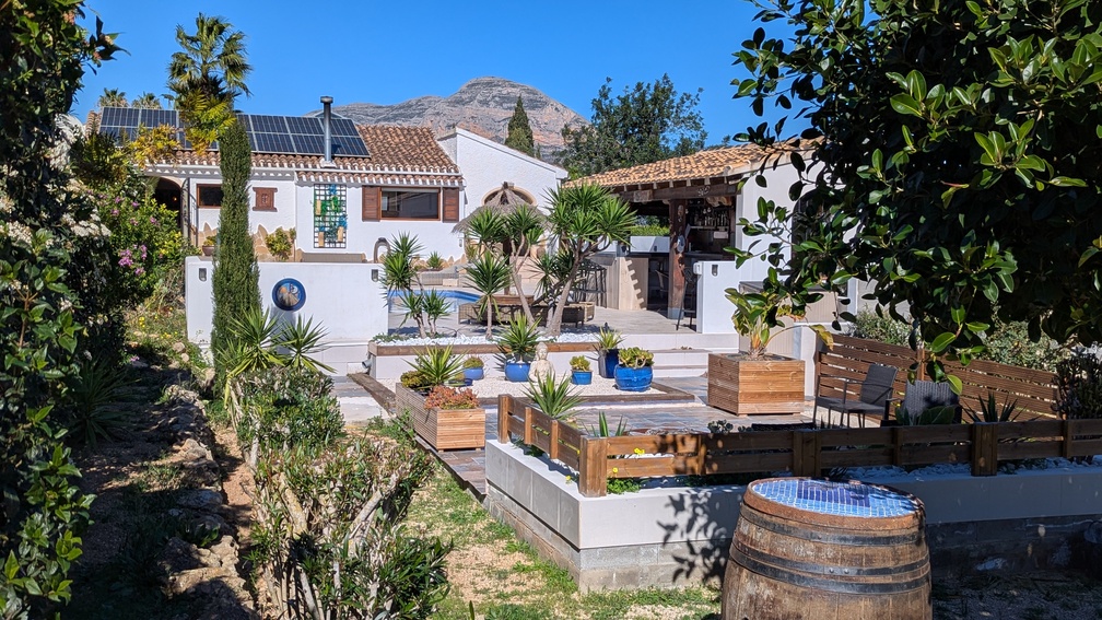 Jardín mediterráneo con terrazas escalonadas, cocina de verano y villa con paneles solares, destacando las vistas panorámicas al macizo del Montgó.