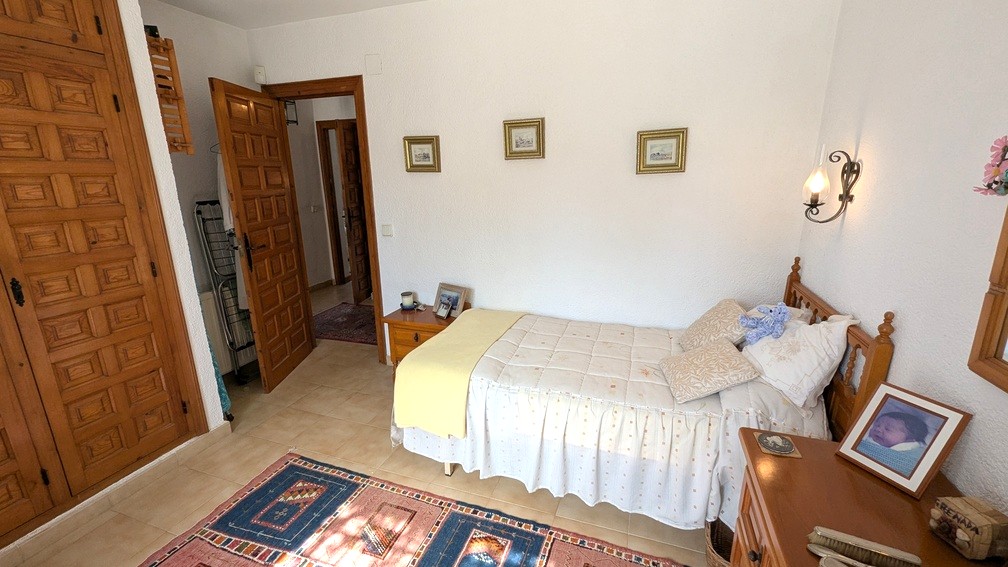 Dormitorio con armarios empotrados de madera tallada, suelos cerámicos y cama individual. Incluye carpintería tradicional y paredes blancas con acabado rugoso.