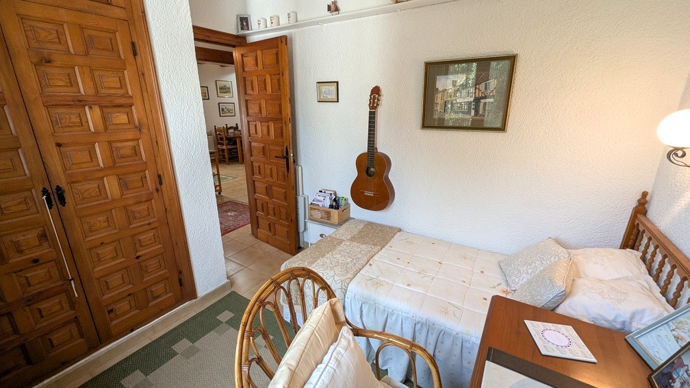 Dormitorio con cama individual, armarios empotrados de madera tallada y paredes blancas con textura. La puerta abierta muestra la conexión con el resto de la vivienda.