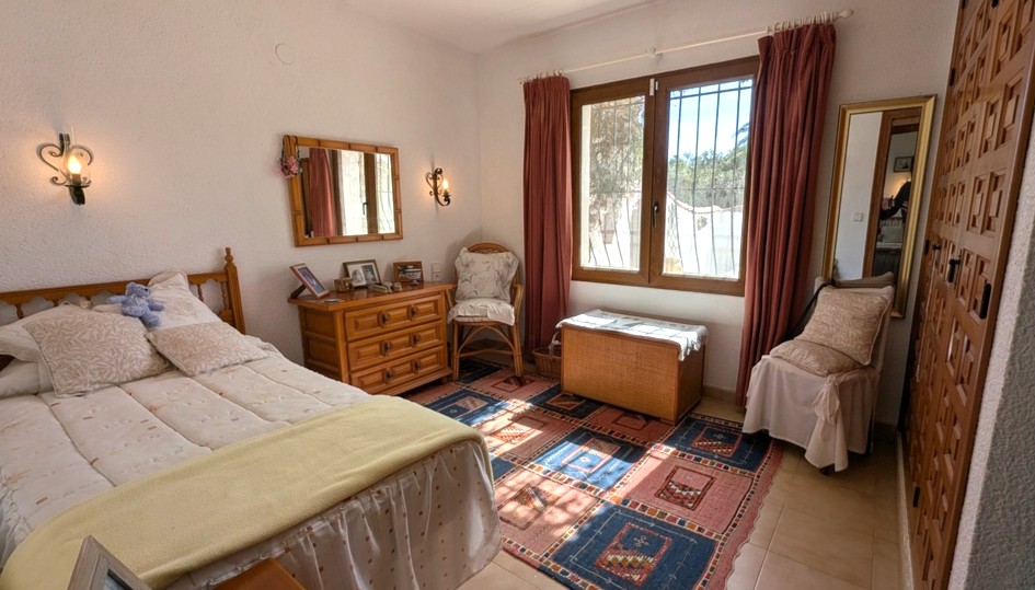 Dormitorio de estilo tradicional con armarios empotrados de madera tallada, cómoda a juego y luz natural. Incluye suelos cerámicos y paredes con textura.