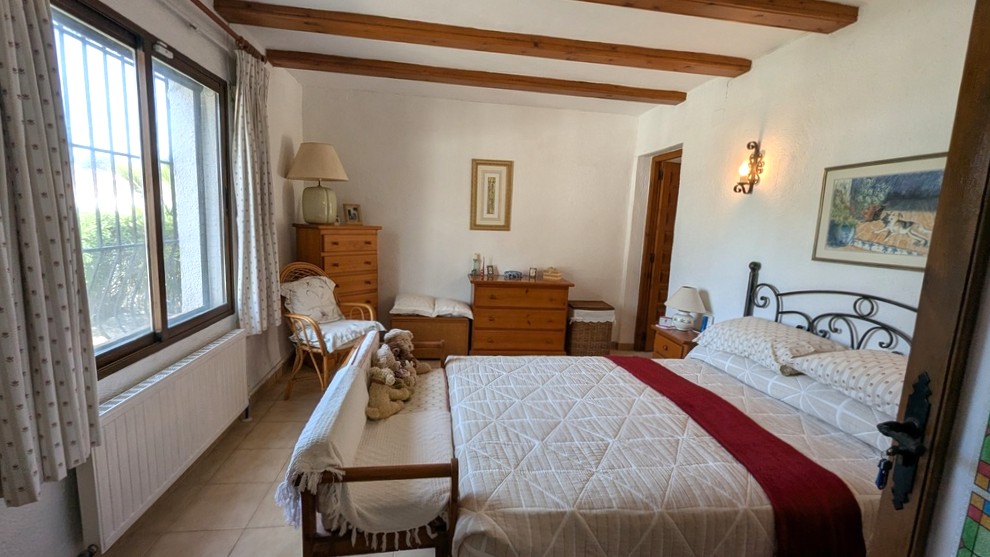 Dormitorio tradicional con vigas de madera vistas, cabecero de forja y mobiliario de madera clásica. La estancia cuenta con luz natural y calefacción por radiador.