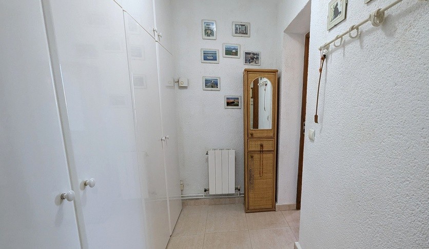 Pasillo o zona de vestidor con amplios armarios empotrados blancos, un mueble de mimbre con espejo y radiador de calefacción central.