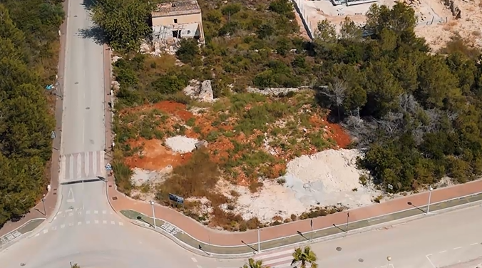 Vista aérea de la parcela de 1.000 m² en esquina, destacando el terreno con tierra rojiza, rodeado de pinos y calles urbanizadas en Villas del Vent.