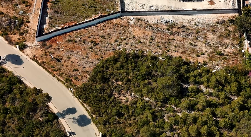 Vista aérea de la parcela de 1.528 m² en Lomas del Rey, mostrando el terreno excavado, el muro de contención perimetral y el acceso directo desde el vial asfaltado.