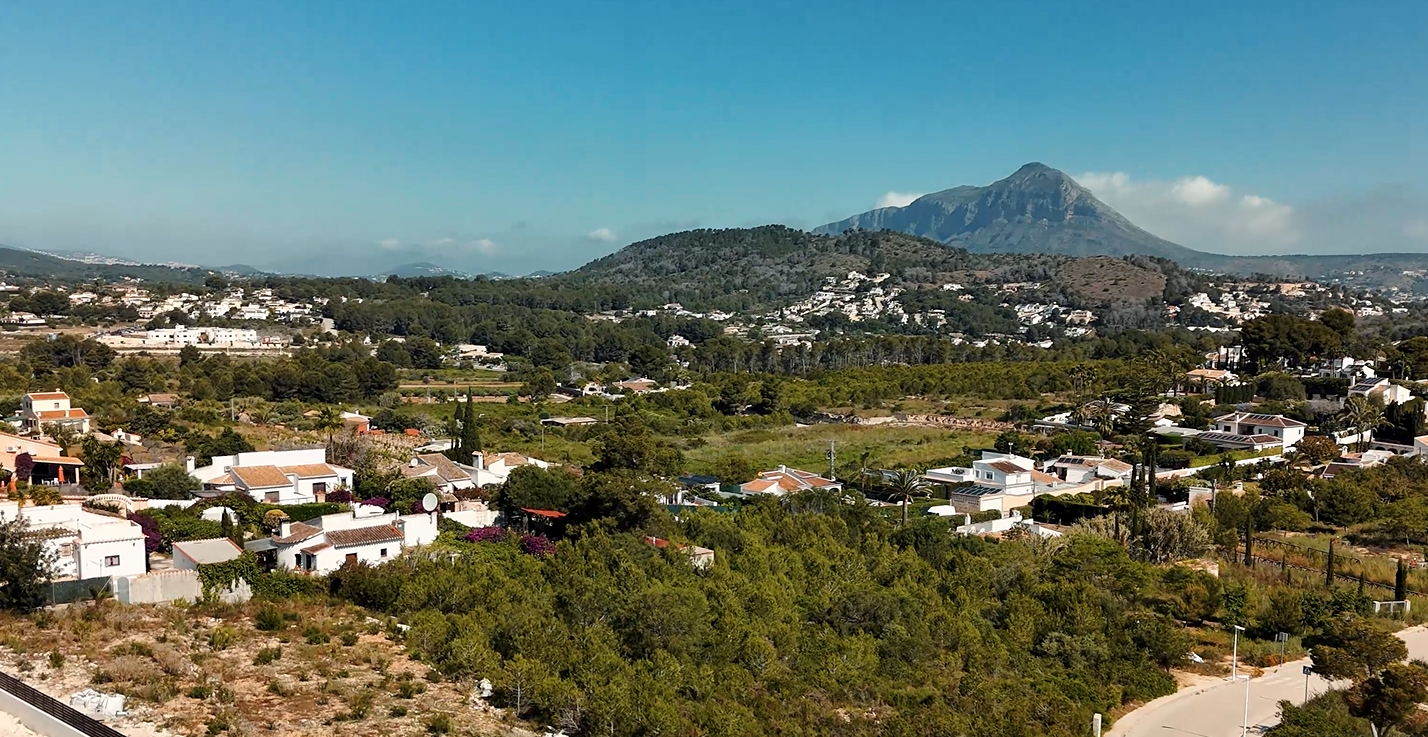 Vista elevada de la urbanización Lomas del Rey en Jávea, con el icónico macizo del Montgó al fondo rodeado de villas mediterráneas y vegetación autóctona.