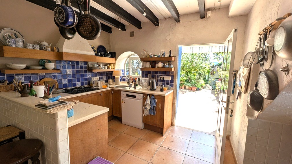 Cocina tradicional con vigas de madera oscura, salpicadero de azulejos azules y mobiliario de madera, con acceso directo a la terraza soleada del jardín.