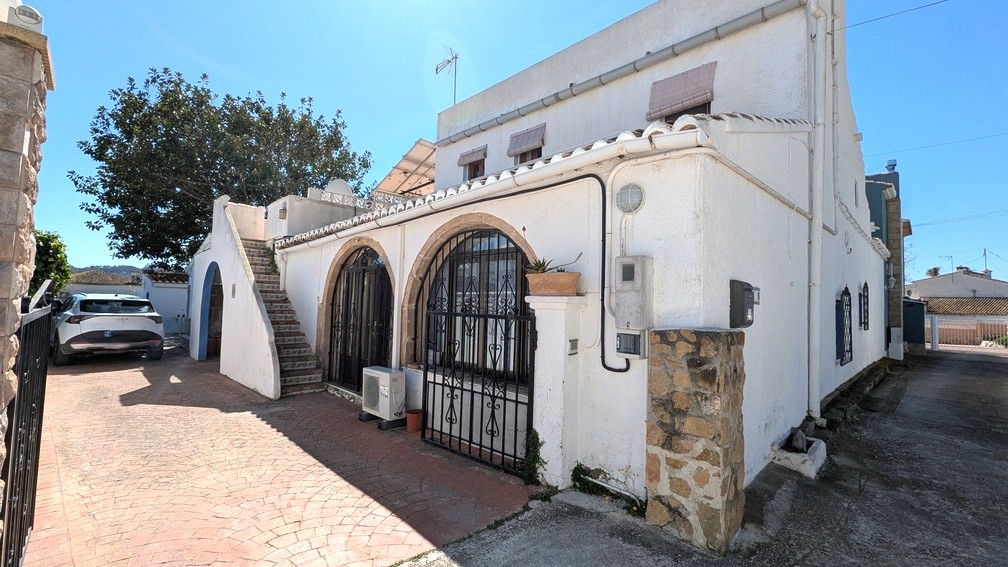 Fachada exterior con arcos de piedra Tosca, rejas de hierro forjado, una escalera exterior decorada con azulejos y paneles solares visibles en la terraza superior.