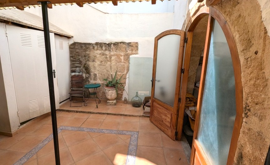Patio tradicional con muros de piedra Tosca original, suelos de terracota con cenefas decorativas y puertas de madera en arco que conectan con el interior.