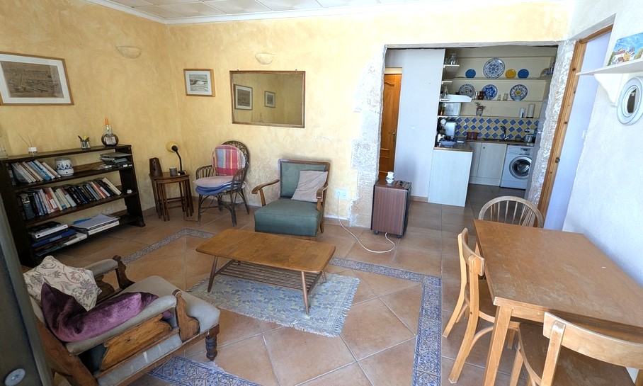 Salón del apartamento de invitados con suelos de terracota y cenefas decorativas, paredes ocres y un arco de piedra tosca que da paso a la cocina integrada.