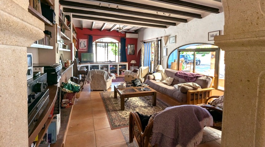 Salón espacioso con vigas de madera oscura, arcos de piedra Tosca, suelos de terracota y grandes ventanales que integran el interior con el exterior.