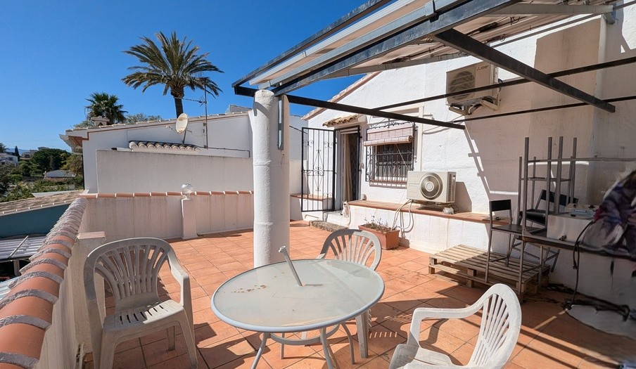 Terraza orientada al sur en la primera planta con suelos de barro, estructura de pérgola metálica y unidades de aire acondicionado exteriores bajo un cielo despejado.