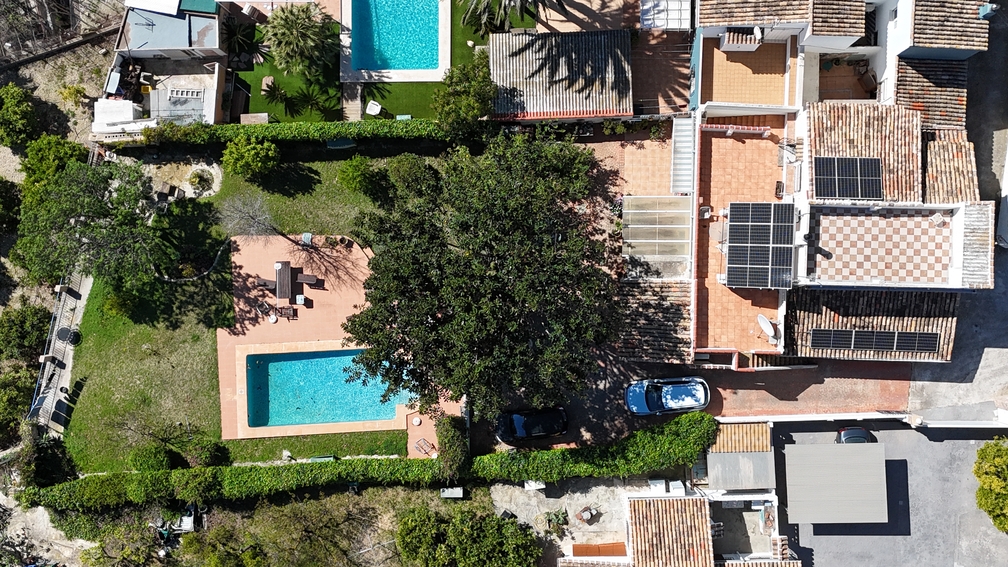 Vista aérea de la villa con piscina privada, jardín y paneles solares instalados en el tejado de teja, rodeada de vegetación mediterránea.